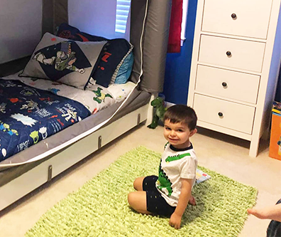 Child playing on a green rug next to the bed